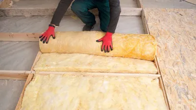 Fiberglass batt insulation roll being installed between joists